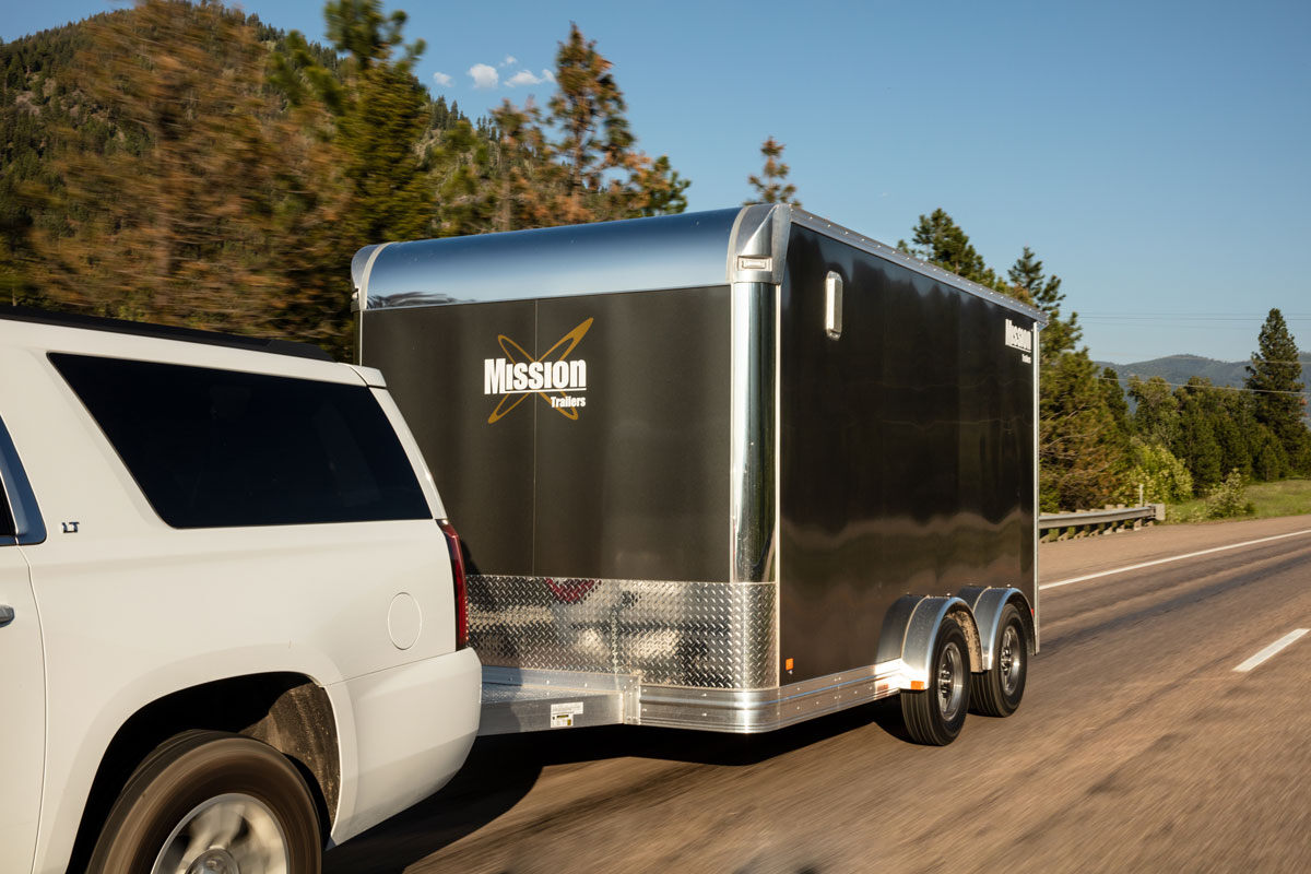 White SUV towing an enclosed aluminum UTV trailer on a road in Montana