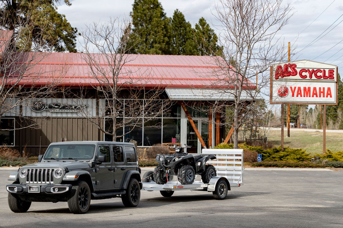 Jeep with open aluminum ATV trailer parked at a shop in Montana.