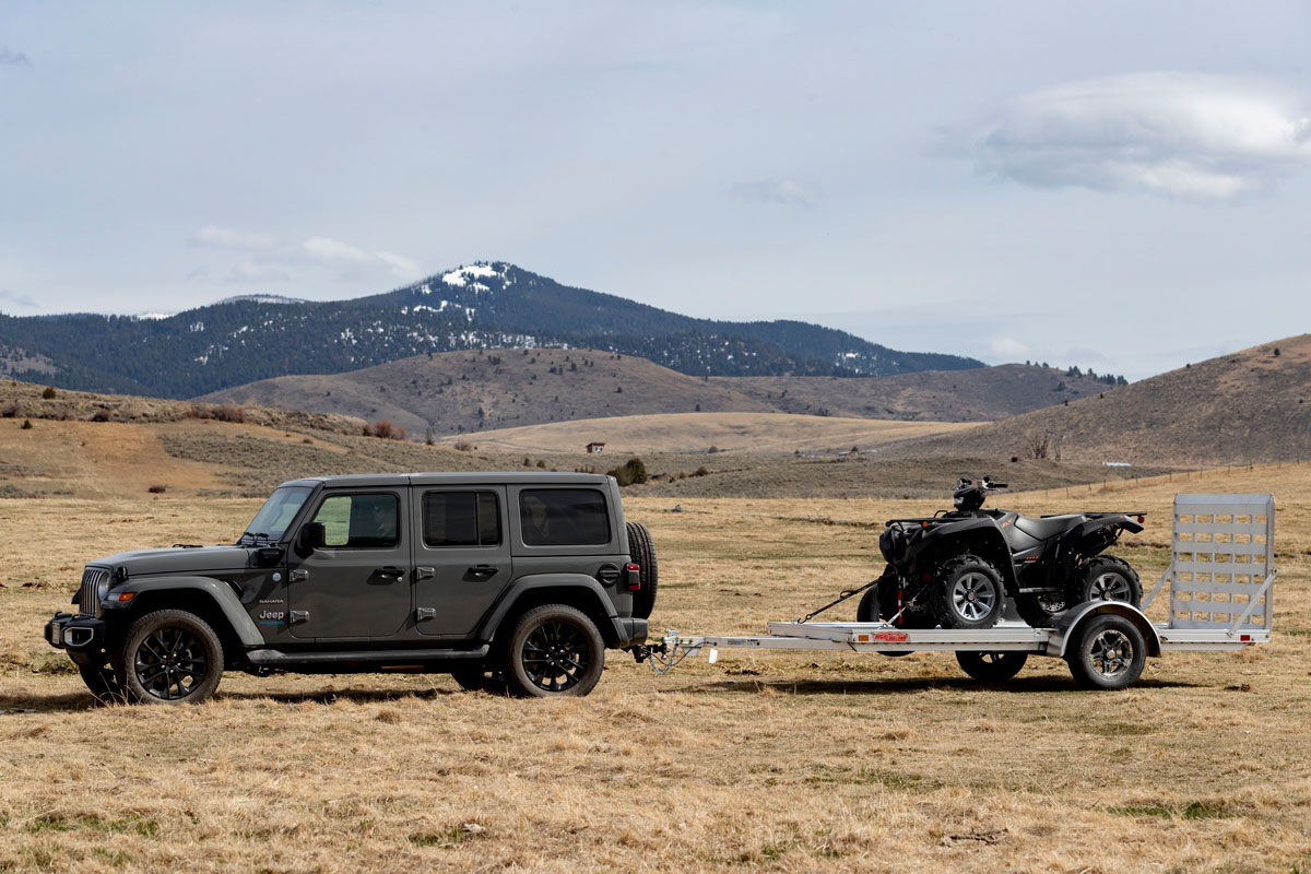 Jeep and open aluminum ATV trailer parked in a field in Montana with a mountain backdrop