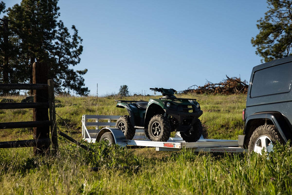 Open aluminum ATV trailer with a four wheeler secured to the deck parked by a fence in Montana