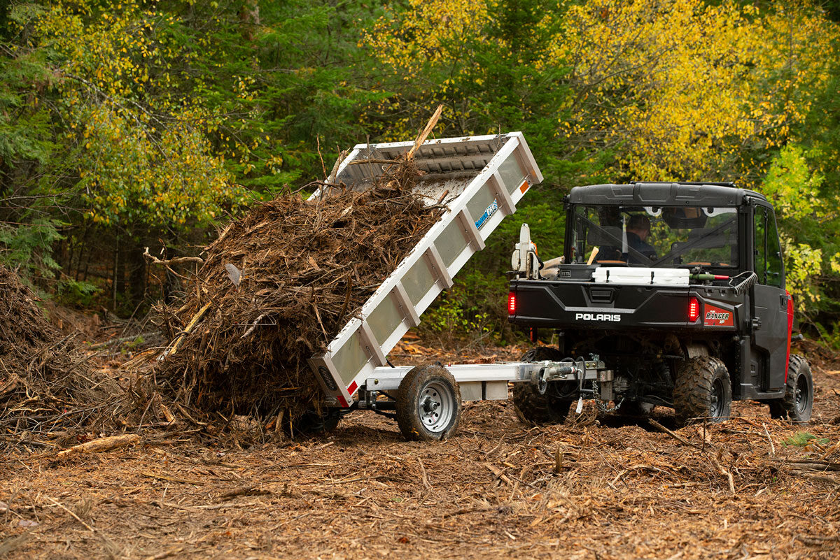 Residential style aluminum dump trailer with tilt system engaged to dump brush onto the ground