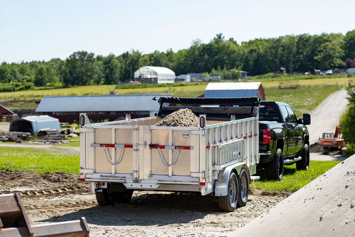 Commercial utility dump trailer from ALCOM full of materials towed by a pickup truck