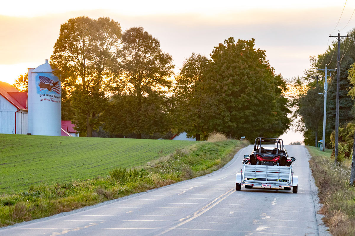 Towing a UTV on an open aluminum trailer past a farm