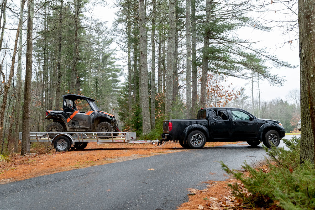 Black pickup truck and open aluminum UTV trailer parked on a driveway