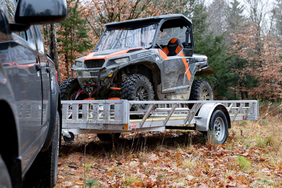 Orange and black UTV secured to a parked aluminum trailer